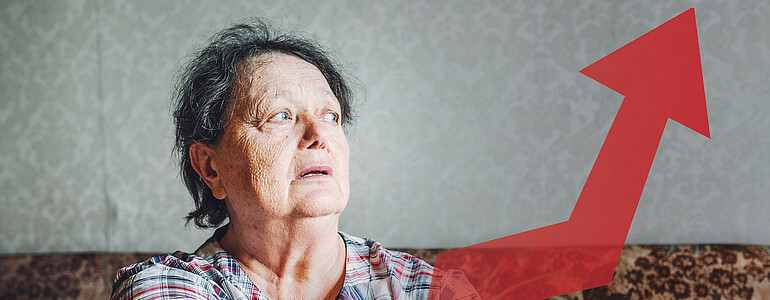 Pensionistin sitzt mit verzweifeltem Blick auf einem Sofa, vor ihr ist ein roter Pfeil der die Teuerung symbolisiert
