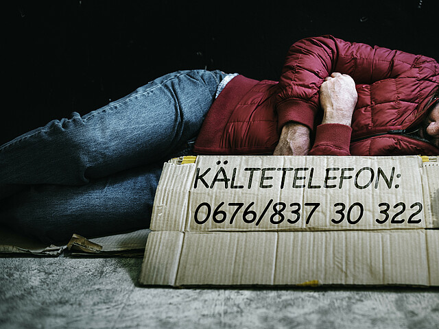 Odachloser auf der Straße mit Telefonnummer vom Kältetelefon der Caritas.