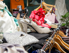 eine Auswahl an glamourösen Schuhen und Taschen im Second-Hand-Laden Carla Oberwart. Zu sehen sind funkelnde High Heels, glänzende Handtaschen und auffällige rote Schuhe. Im Hintergrund sind Kleiderbügel und weitere Accessoires zu erkennen.