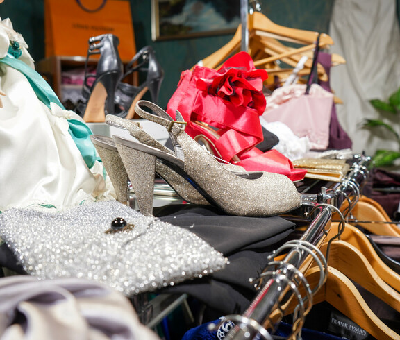 eine Auswahl an glamourösen Schuhen und Taschen im Second-Hand-Laden Carla Oberwart. Zu sehen sind funkelnde High Heels, glänzende Handtaschen und auffällige rote Schuhe. Im Hintergrund sind Kleiderbügel und weitere Accessoires zu erkennen.