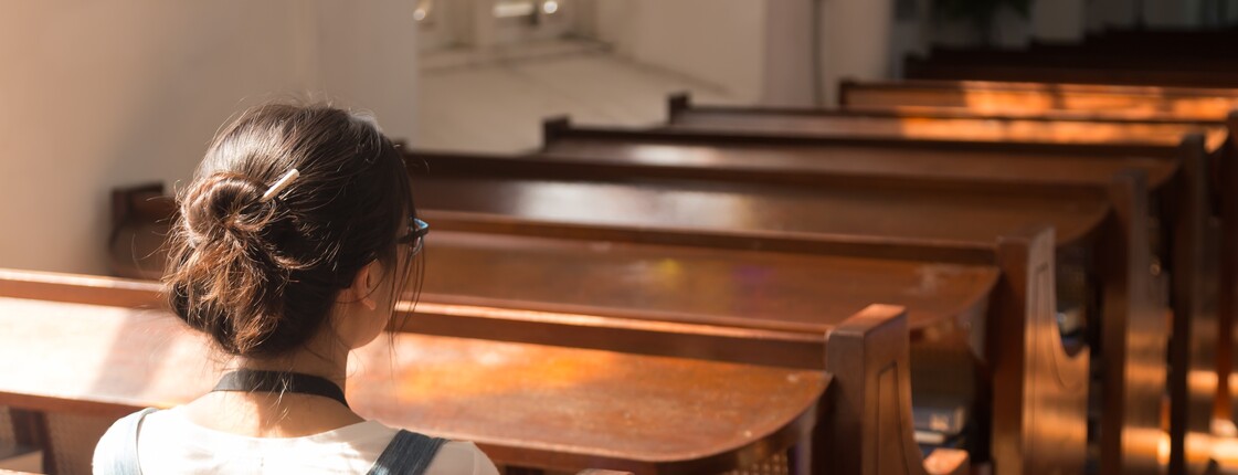 Junge Frau sitzt in der Kirche  Eine junge Frau sitzt in der Kirche. Ihr Gesicht ist nicht zu erkennen.