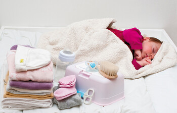 Ein Baby liegt auf einer Decke, daneben Windeln, Hygieneartikel und Kleidung.