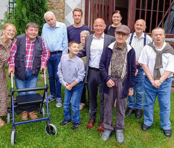 Die Bewohner*innen des Haus St. Stephan stehen auf einer Wiese und lächeln in die Kamera.