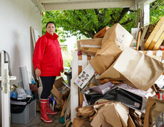 Melanie Balaskovics steht neben einem Stapel beschädigter Kartons und Habseligkeiten unter einem Vordach, umgeben von Aufräumarbeiten nach einem Hochwasser.