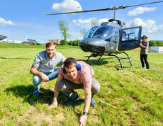 Ein Bewohner und Betreuer aus dem Haus St. Stephan knien auf einer grünen Wiese vor einem gelandeten Hubschrauber, während eine weitere Person neben der geöffneten Tür des Hubschraubers steht.