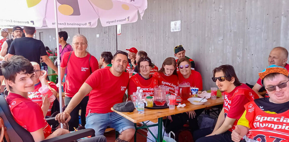 Das Haus St. Stephan nahm an den Special Olympics teil. Sie sitzen an einen Tisch herum und genießen eine Pause. Auf dem Tisch sind Getränke und Snacks zu sehen, und im Hintergrund gibt es weitere Teilnehmer.