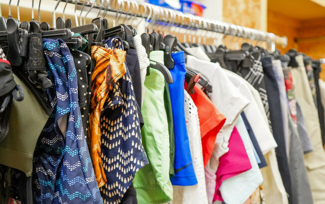 eine Kleiderstange im Second-Hand-Laden Carla Eisenstadt, auf der verschiedene bunte Kleidungsstücke, darunter Blusen, Hemden und T-Shirts, ordentlich aufgehängt sind.