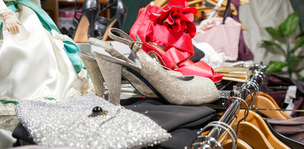 eine Auswahl an glamourösen Schuhen und Taschen im Second-Hand-Laden Carla Oberwart. Zu sehen sind funkelnde High Heels, glänzende Handtaschen und auffällige rote Schuhe. Im Hintergrund sind Kleiderbügel und weitere Accessoires zu erkennen.